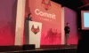 Two people standing on a stage at a conference.