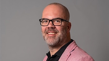 A bald man wearing glasses and a pink jacket.