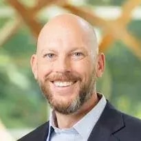 A bald man smiling in front of a wooden wall.